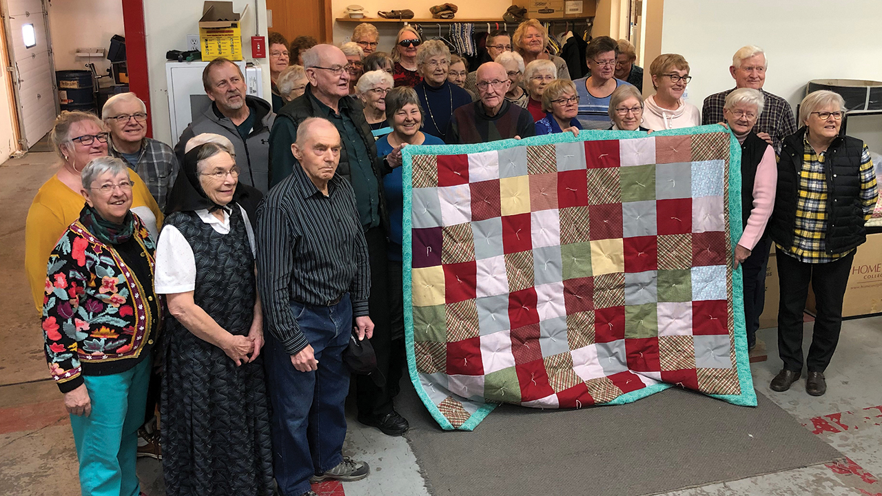 A group of volunteers display a blanket they made during a Great Winter Warm-up event on Jan. 20, 2020, at the Mennonite Central Committee Material Resources Centre in Plum Coulee, Man. Together the group finished 150 comforters for delivery to families who have been displaced by conflict or disaster. — Mennonite Central Committee