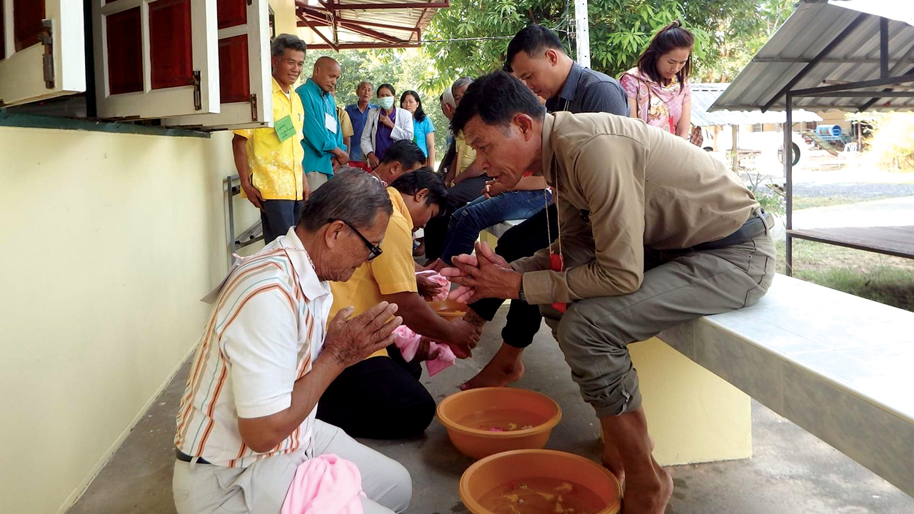 Sawang Phumewatthana, left, a lay leader of Sripuppa Living Water Church in Roi Et province, Thailand, prepares to wash the feet of Sa-nga Inchai, sitting on the bench. — Pat and Rad Houmphan