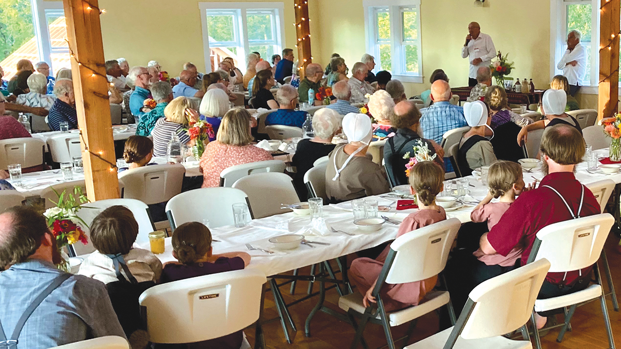 Bob Buxman speaks about Mennonite Central Committee as Clark Yoder, right, listens at an Amish dinner that raised $10,875 for MCC and Mennonite Disaster Service on Aug. 9 at Morning Shade Farm near Canby, Ore. — Jim Pauls