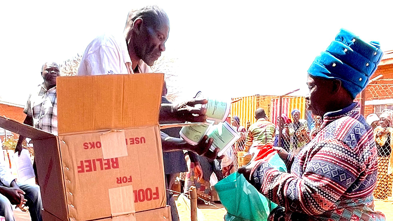 Phineas Zavian, from the Mennonite Brethren Church in Malawi, packs canned meat into a bag for Fatima Filamani at a distribution in the Dzaleka Refugee Camp in 2024. — Eldon Wagler/MCC